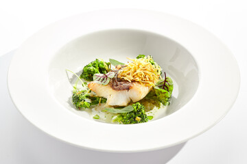 Panfried Fish with broccoli and cream sauce. Healthy roasted cod with green leaves. Fried Fish on white restaurant plate isolated on white background.