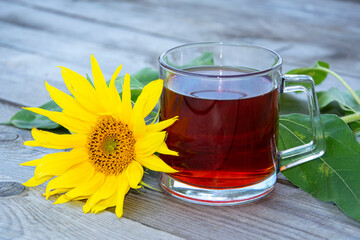 Mug with tea and sunflower flower on a wooden background. Tea in a glass cup.