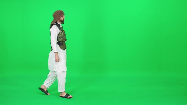 A man of Arab appearance in traditional clothes walking down the street against the green background, man in military equipment, chromakey template.