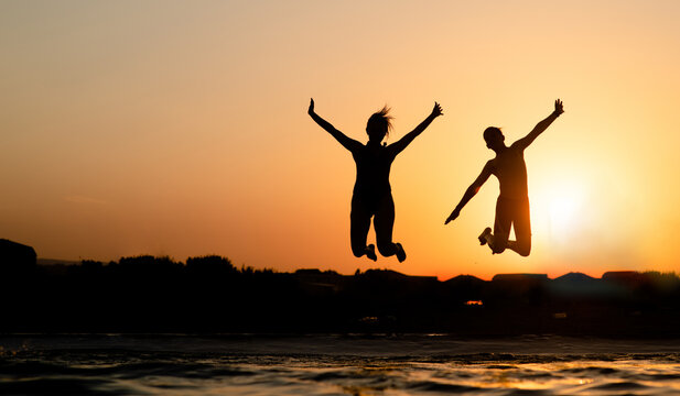 Happy kids are having fun and jump at sunset beach in sunlight. Empty space for text