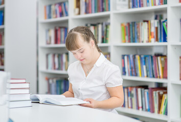 Smart young girl with syndrome down reads a book at library. Education for disabled children concept