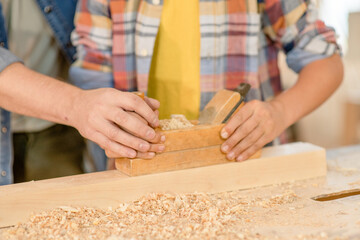 Close up father teaches son to plan a wooden block