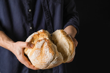 Male baker with fresh bread on dark background, closeup