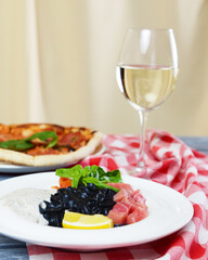 Squid Ink Black Pasta with seafood served on a white plate with a glass of white wine.