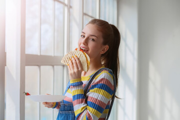 Beautiful young woman eating tasty quesadilla at home