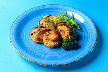Delicious grilled vegetables served on a blue plate over blue background. BBQ Grill concept.