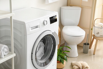 Modern washing machine with laundry in bathroom