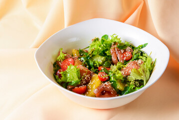 Fresh salad with shrimp and vegetables close up in a bowl over pastel yellow or golden background.
