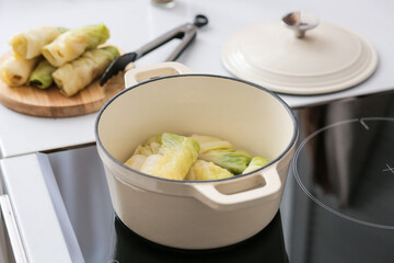 Cooking pot with raw stuffed cabbage rolls on electric stove at kitchen
