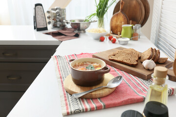 Cooking pot with tasty sauerkraut soup and slices of fresh bread on table in kitchen