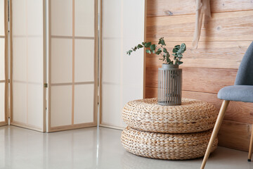 Vase with plant branches on pouf near folding screen