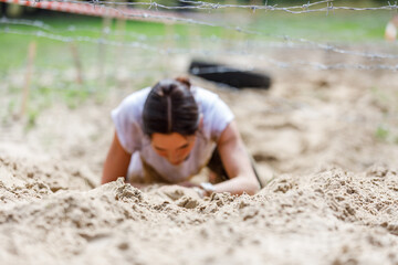 Young sportswoman crawling under barbed wire on her obstacle race course