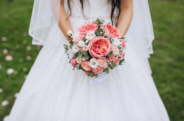 A bride in a white dress holds a bouquet of roses and wildflowers. Wedding photography.