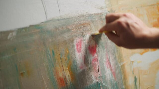 Creating an abstract painting, a talented man artist covers the canvas with oil paint, priming and draws the background, close-up view of the hands, 4k slow motion.