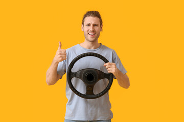 Young man with steering wheel showing thumb-up on color background