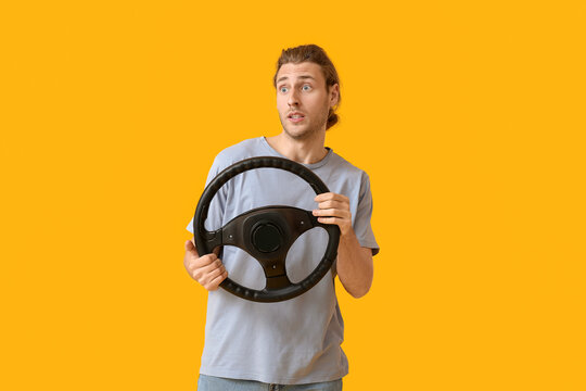 Shocked young man with steering wheel on color background