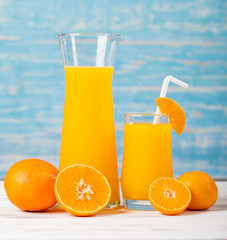 Fresh orange juice in jar and glass decorating with straw and fresh orange on white wooden table on blue wall. Studio picture concept for healthy diet