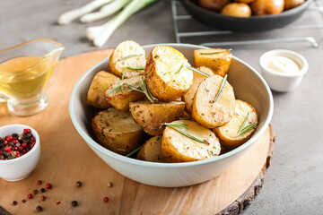 Bowl with baked potatoes and rosemary on grey background