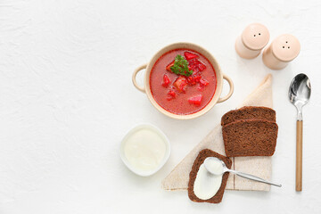 Pot with tasty borscht, sour cream and bread on light background