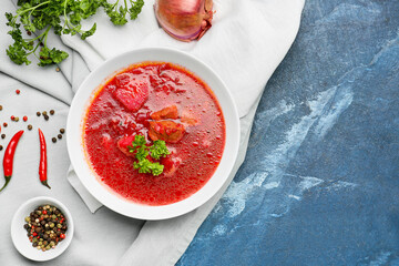 Bowl with tasty borscht, onion, parsley and peppercorns on color background