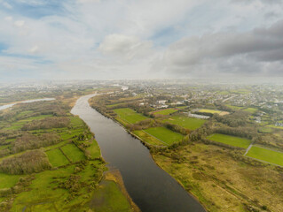 Fototapeta na wymiar Aerial drone view on river Corrib, Galway city, Ireland. Park and sports ground for Irish National sports hurling, camogie, rugby on the right. Cloudy sky