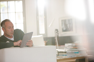 Older man using digital tablet on living room sofa