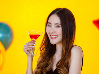 Close up shot of Asian pretty long hair girl in sexy dress standing sipping drinking red cocktail beverage alcohol drink in tall glass in front colorful balloons on blurred yellow background in party