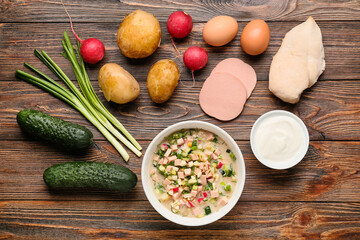 Bowl with tasty okroshka and ingredients on wooden background