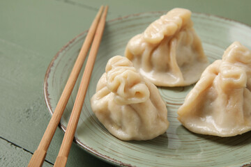 Plate with tasty dumplings and chopsticks on color wooden background, closeup
