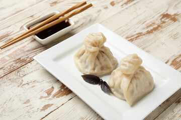 Plate with tasty dumplings, chopsticks and bowl of sauce on light wooden background, closeup