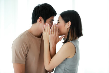 Portrait shot of young Asian lover couple standing closely and looking at each other eyes while showing a golden engagement rings that wore in their ring fingers on white background