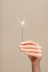 New year sparkler in female hand on beige background. Woman hold glowing holiday sparkling fireworks