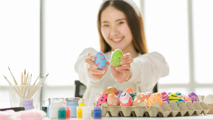 Fototapeta na wymiar A cute young and beautiful Asian woman wearing bunny rabbit ears headband showing hand made painted easter eggs with happy and smile face