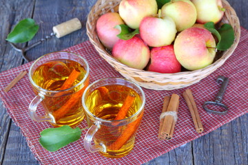 Apple cider in glass mugs near wicker basket with fresh fruit on the old wooden table. 