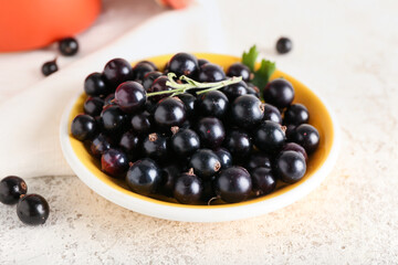 Bowl with ripe black currant on light background