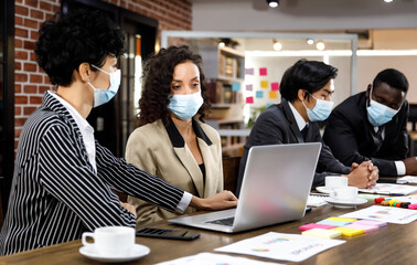 Multiracial mixed race businesspeople group working with concentration  at office, wearing face masks as new normal to protect or prevent virus in pandemic crisis, using laptop and job discussion.