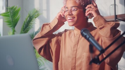 Beautiful young dark skinned woman making a podcast recording for her online show. Close up of stylish happy millennial african american woman wearing headphones earphones for radio program.