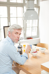 Older man reading newspaper at breakfast table