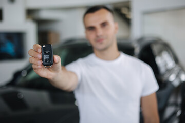 Fototapeta na wymiar Portrait of handosom man in car showroom. Man hold keys from her new car. Keys in focus