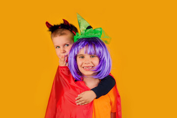 One little toddler boy and girl in a carnival costume for Halloween is isolated on a yellow background. Traditions, holidays concept.