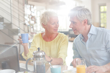 Fototapeta na wymiar Older couple laughing together at breakfast table with laptop