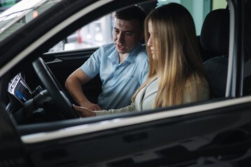 Obraz na płótnie Canvas Bussines woman choosing car i car showroom. Salesperson sitting in car with customer and show desing