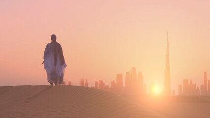 Arabic woman weared in traditional UAE dress - abayain looks on the sunset at a desert with Dubai city silhouette on the background.