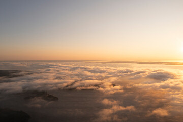 Fototapeta premium Aerial top view gold sunrise over clouds in blue sky. Aerial top view cloudscape. Texture of clouds. View from above. Orange sunrise or sunset over clouds. Panorama clouds texture