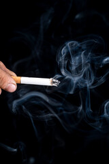 Black background. the hand of a man with roughened skin holds a cigarette. blue smoke is coming from it. close-up.