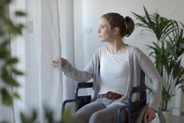 Sad woman in wheelchair looking outside