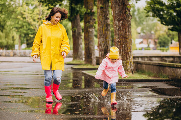 Mother with daughter having fun jumping in puddles