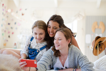 Obraz premium Three teenage girls using smart phone together while lying on bed