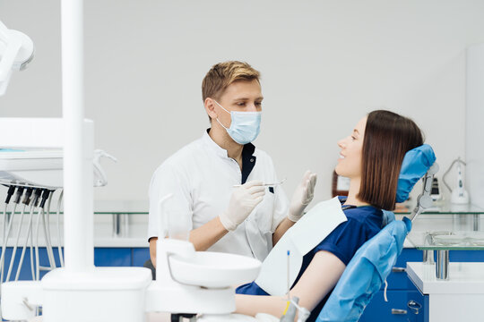 Caucasian male dentist examining young woman patient's teeth at dental clinic. Doctor probing teeth with dental instrument using an explorer look for cavities treatment and checking problems