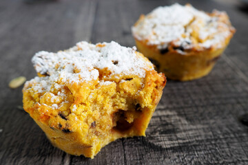 half a bitten pumpkin muffin and one whole gluten-free muffin, sprinkled with powdered sugar, are lying on a wooden table . side view